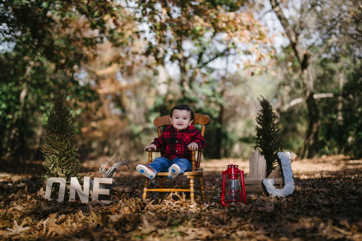 Baby one year picture in rocking chair one in a forrest of leaves with photography props at Denman Estate Park in San Antonio
