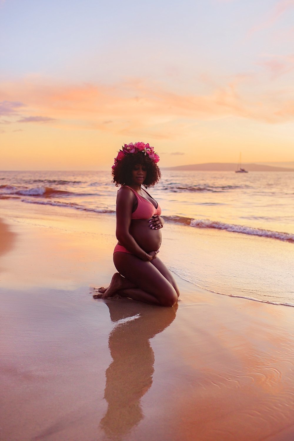 Gorgeous woman with bright pink floral headpiece looks at the camera during her babymoon session at sunset photographed by Love + Water