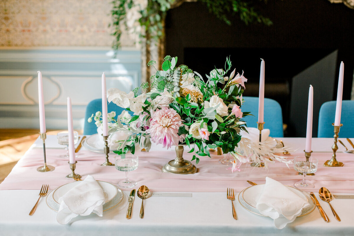 Tablescape with a lush blush floral centerpiece, tapers, golden cutlery, and vintage napkins for an intimate wedding photoshoot at the Tassenmuseum organized by Lovely & Planned