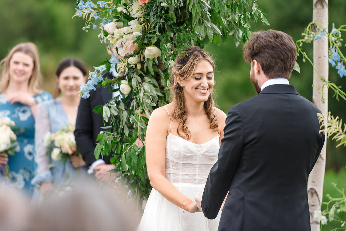 A bride and groom holding hands during their wedding ceremony, with bridesmaids in the background.