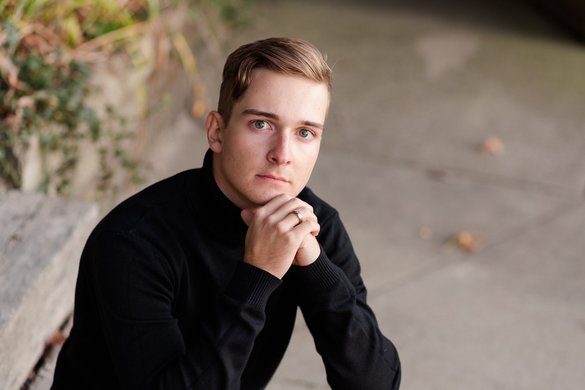 perry high school senior guy sitting on wooden steps, wearing black sweater, with arms on his knees with hands under his chin, looking at camera with a serious face, photographed at Sippo Lake, photographed by Jamie Lynette Photography Canton Ohio Senior Photographer