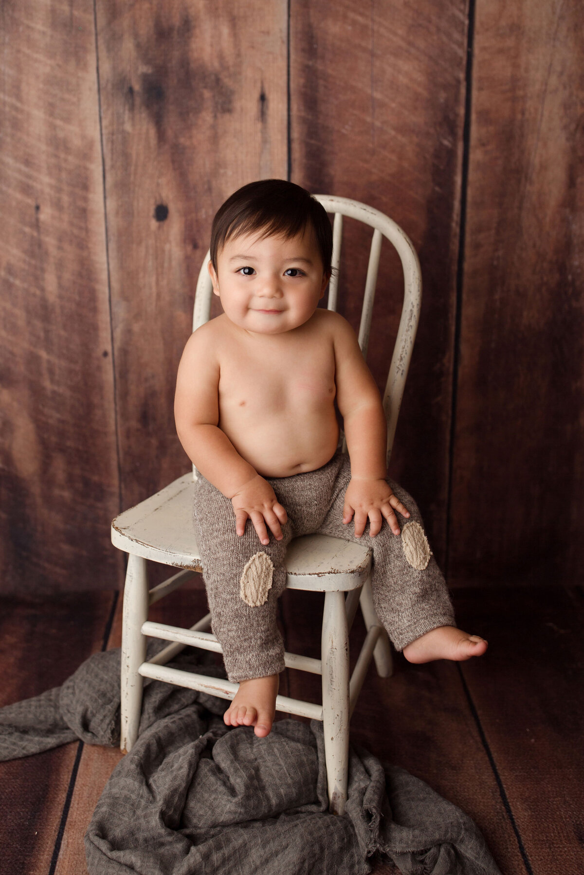 1 year old kid sitting on  a chair wearing pants with patches