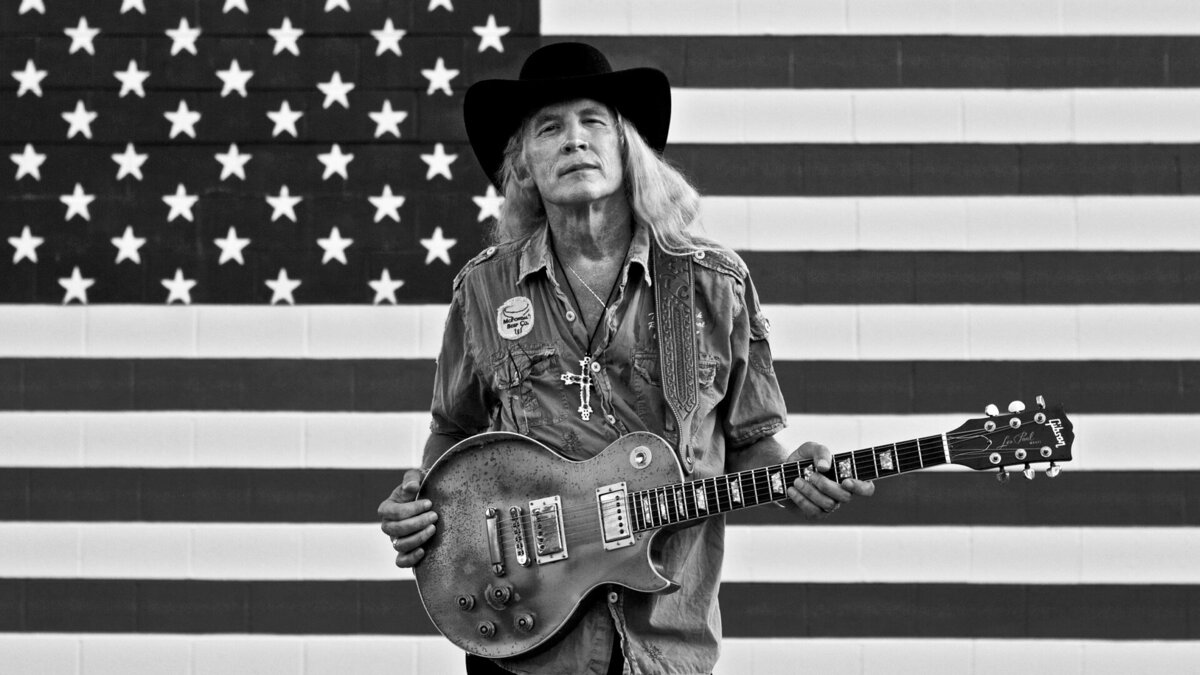 Country Music Portrait Billy Crain black and white standing against American Flag with guitar and black cowboy hat