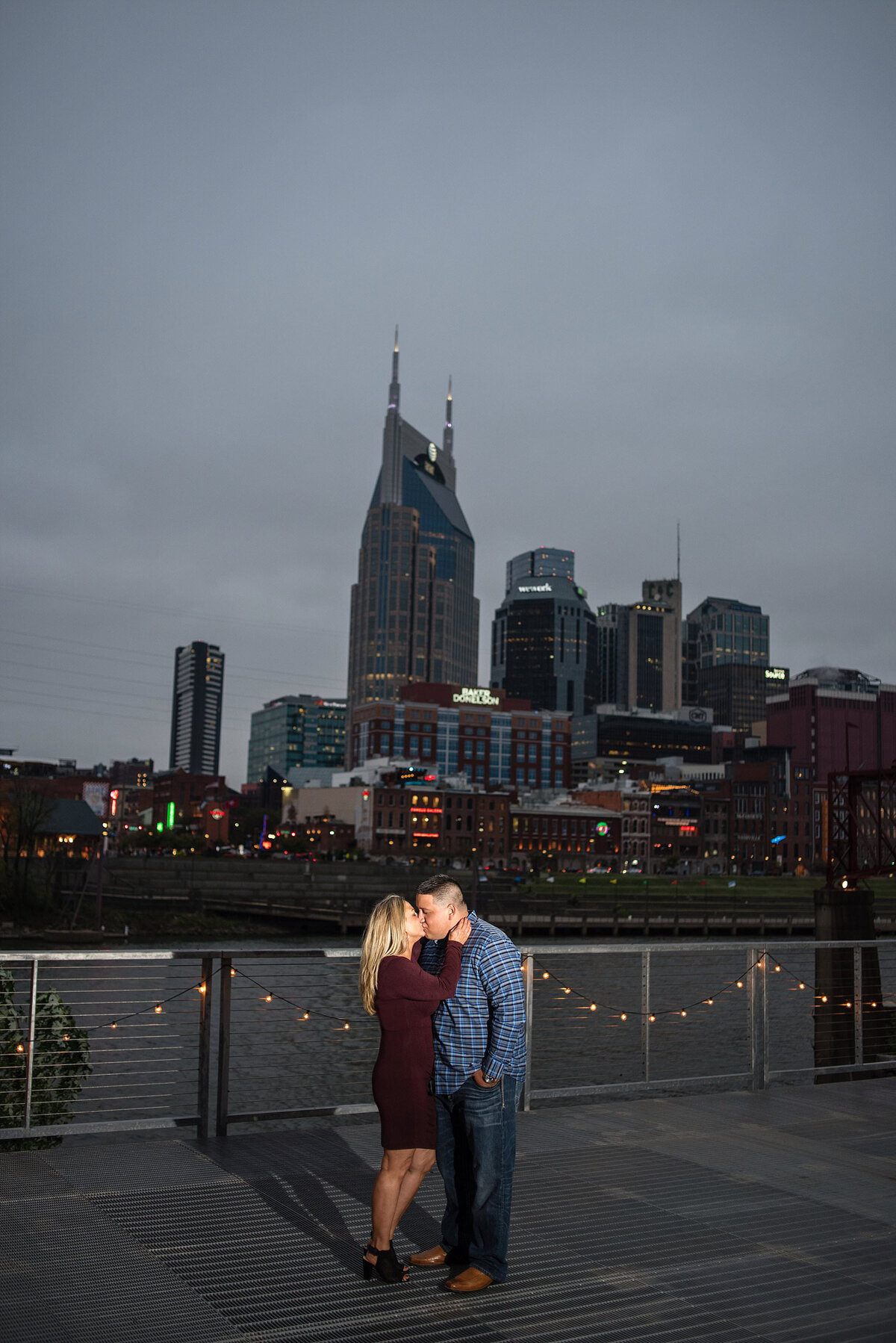 Couple sharing a kiss alongside the Cumberland river on a stormy night with the Nashville skyline behind them