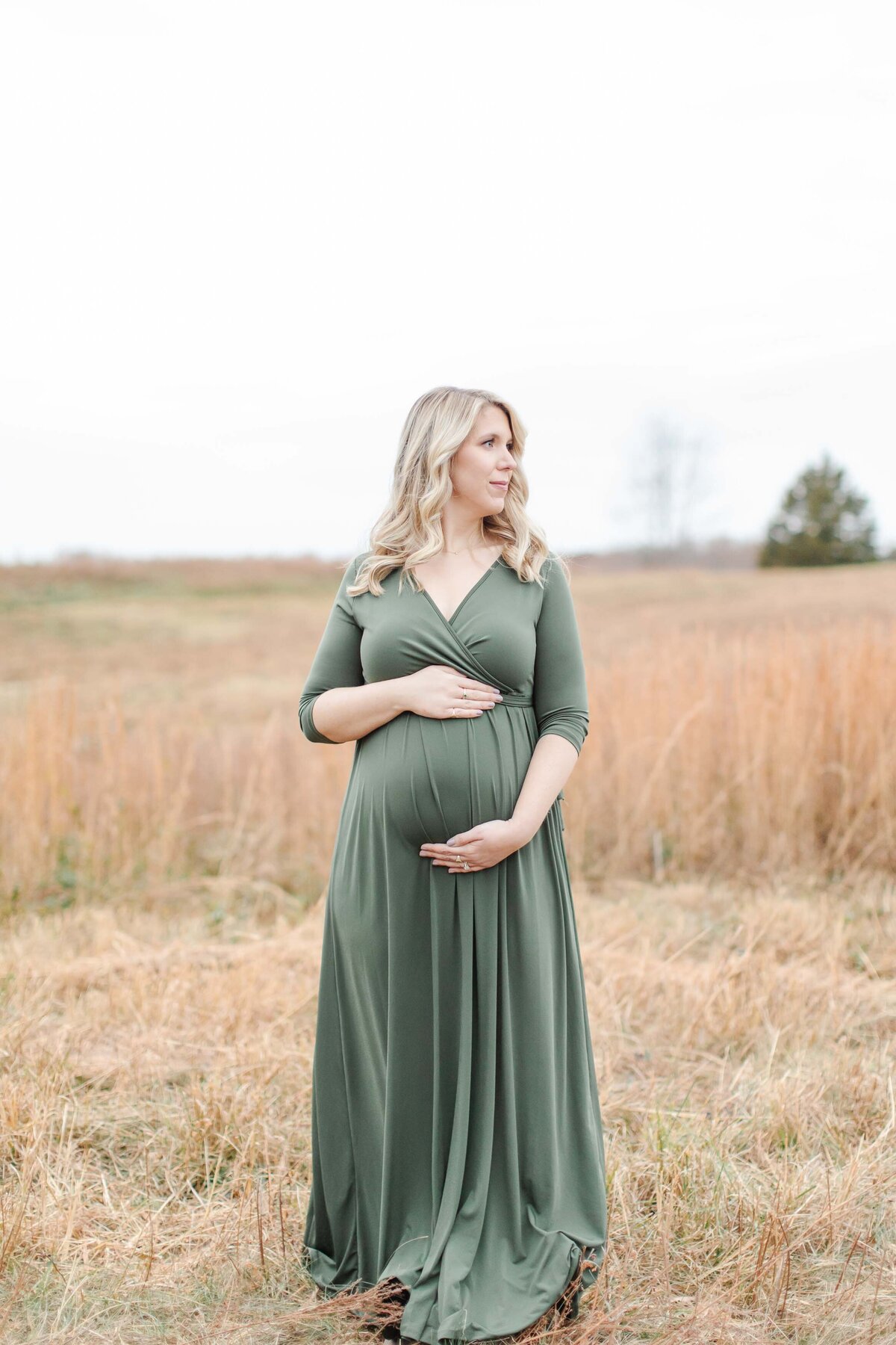 woman standing in field with green dress and baby bump with photographer in Norhtern Virginia