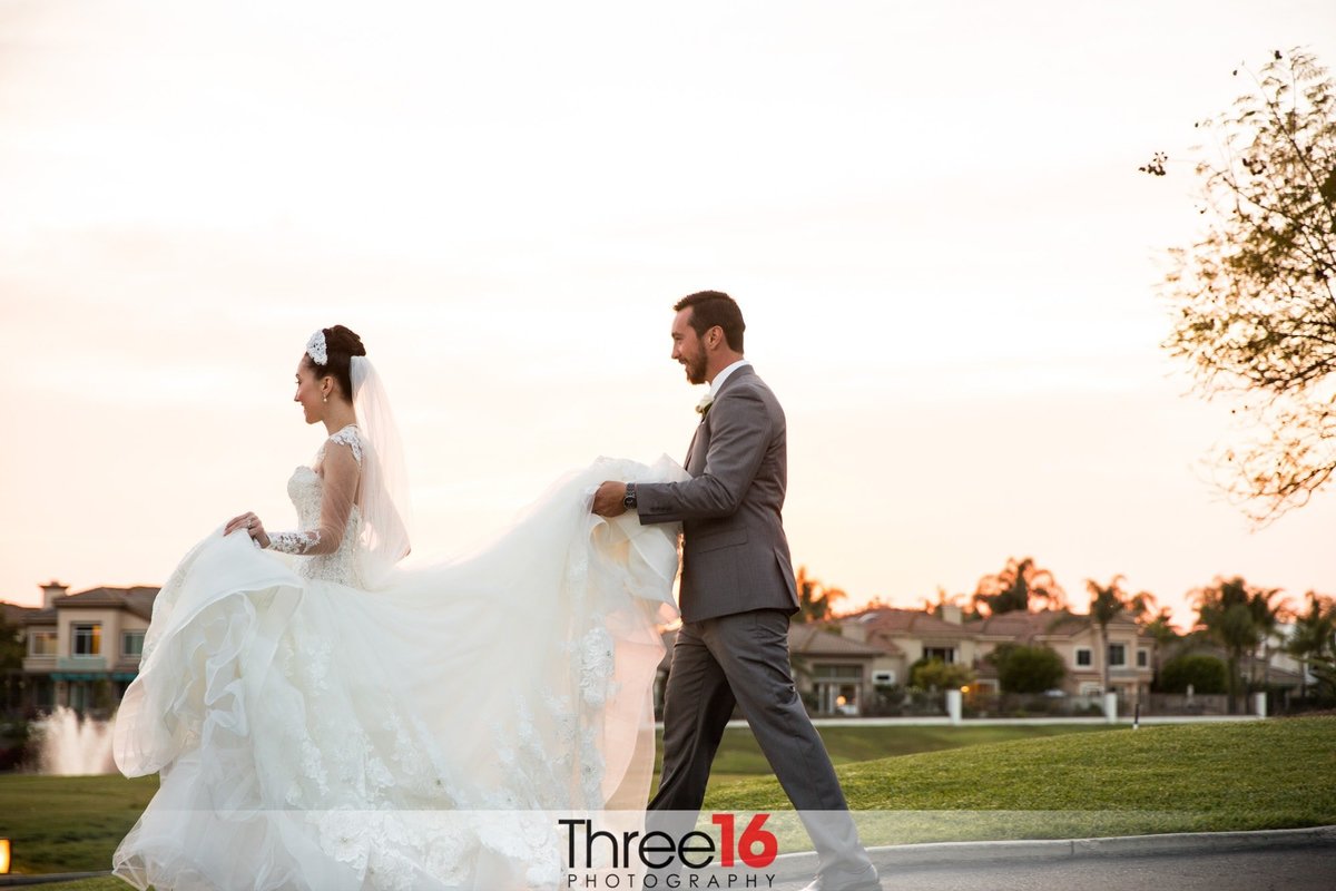 Groom carries his Brides dress train as they walk across the Tustin Ranch Golf Club golf course