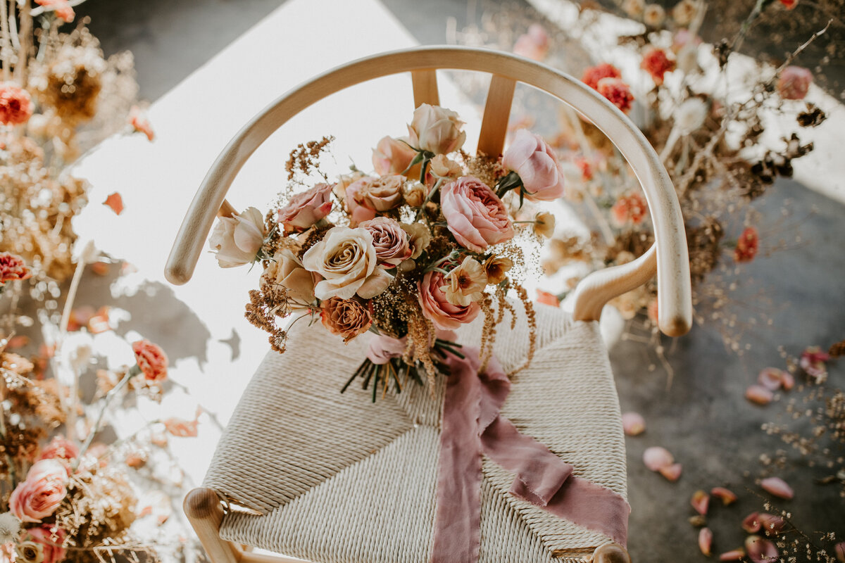 Light-colored wishbone chair with a pink and ivory bouquet surrounded by blush and ivory flower arrangements.