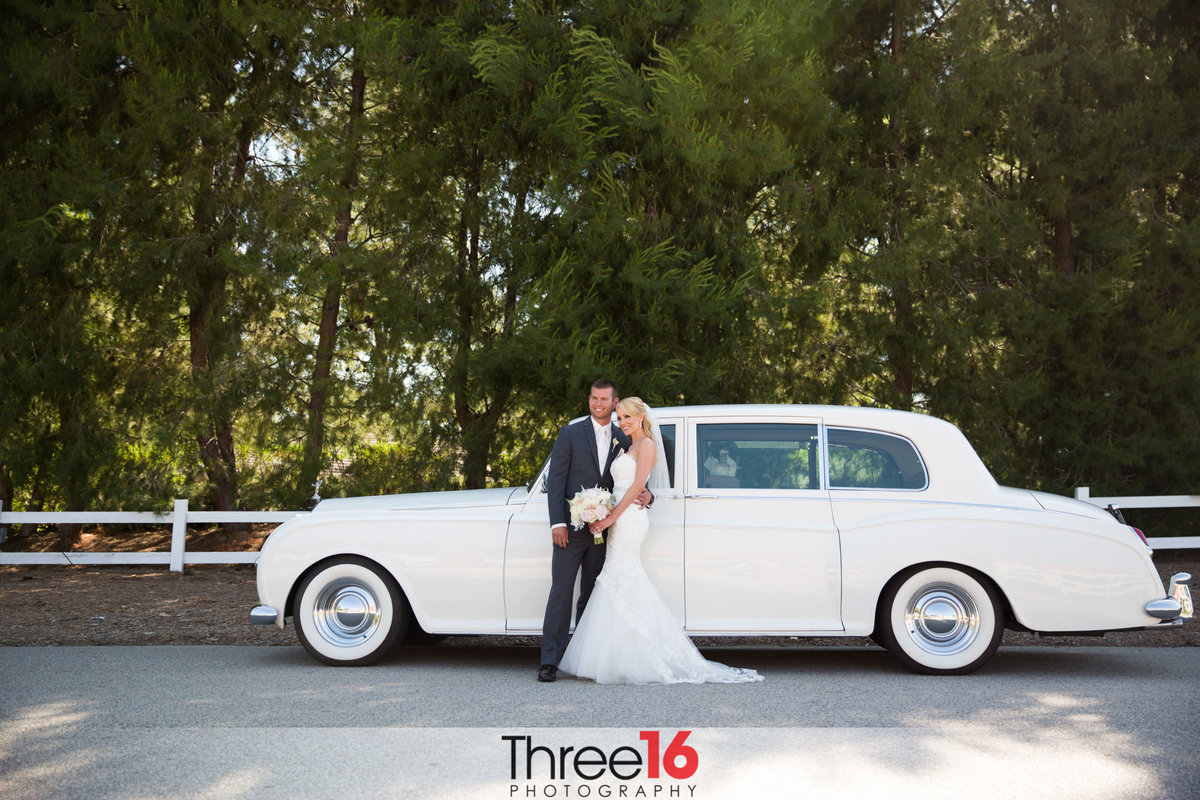 Newly married couple pose together in front of a vintage classic car