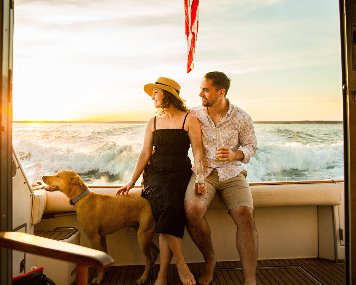 A man and woman sit with their dog on a boat during their engagement session.