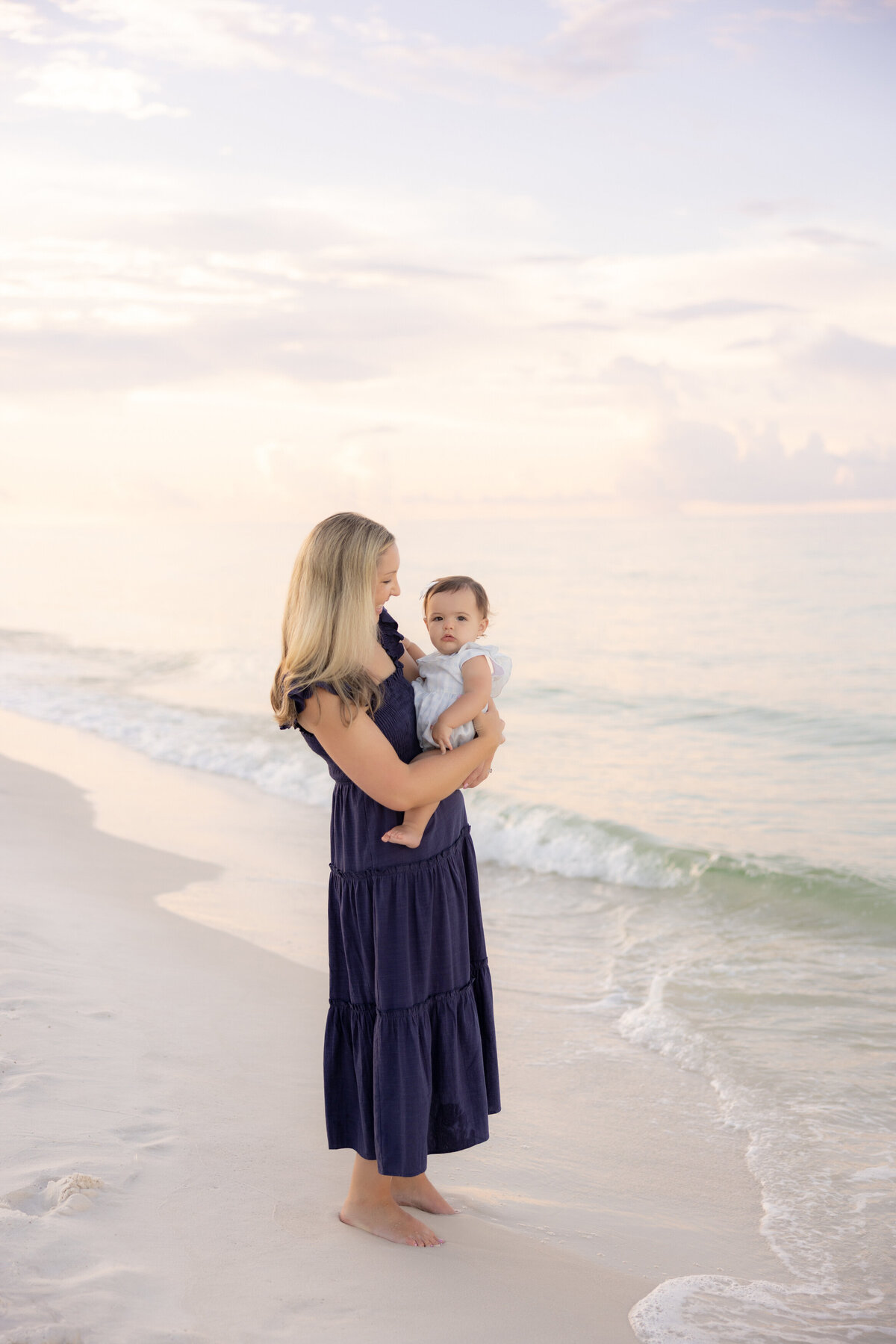 A mom holding their baby while standing at the water's edge near Watercolor Inn.