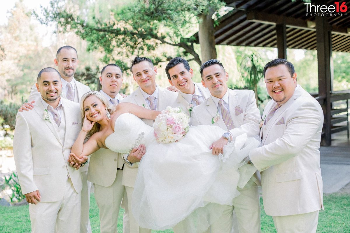 Groomsmen lift and hold up the Bride as she poses for photos