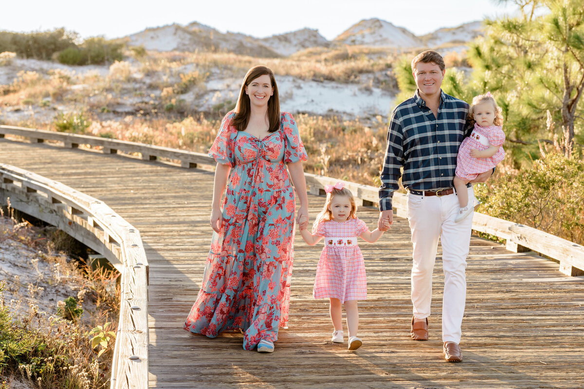 Two parents holding one child's hand while one holds a small baby