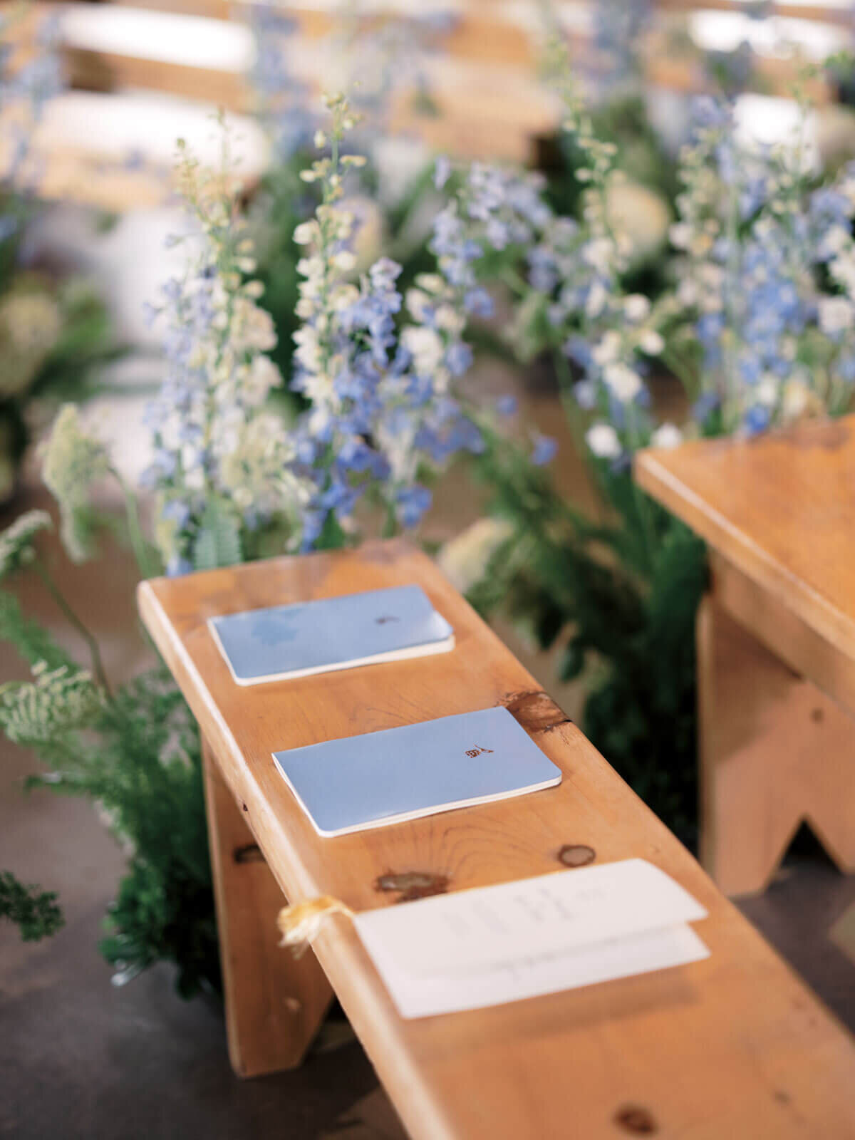 Small blue and white booklets are in a wooden slab chair for the wedding at The Lion Rock Farm, CT. Image by Jenny Fu Studio