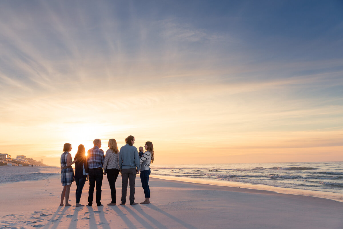 A family standing in a line at a beach with the sun setting behind them