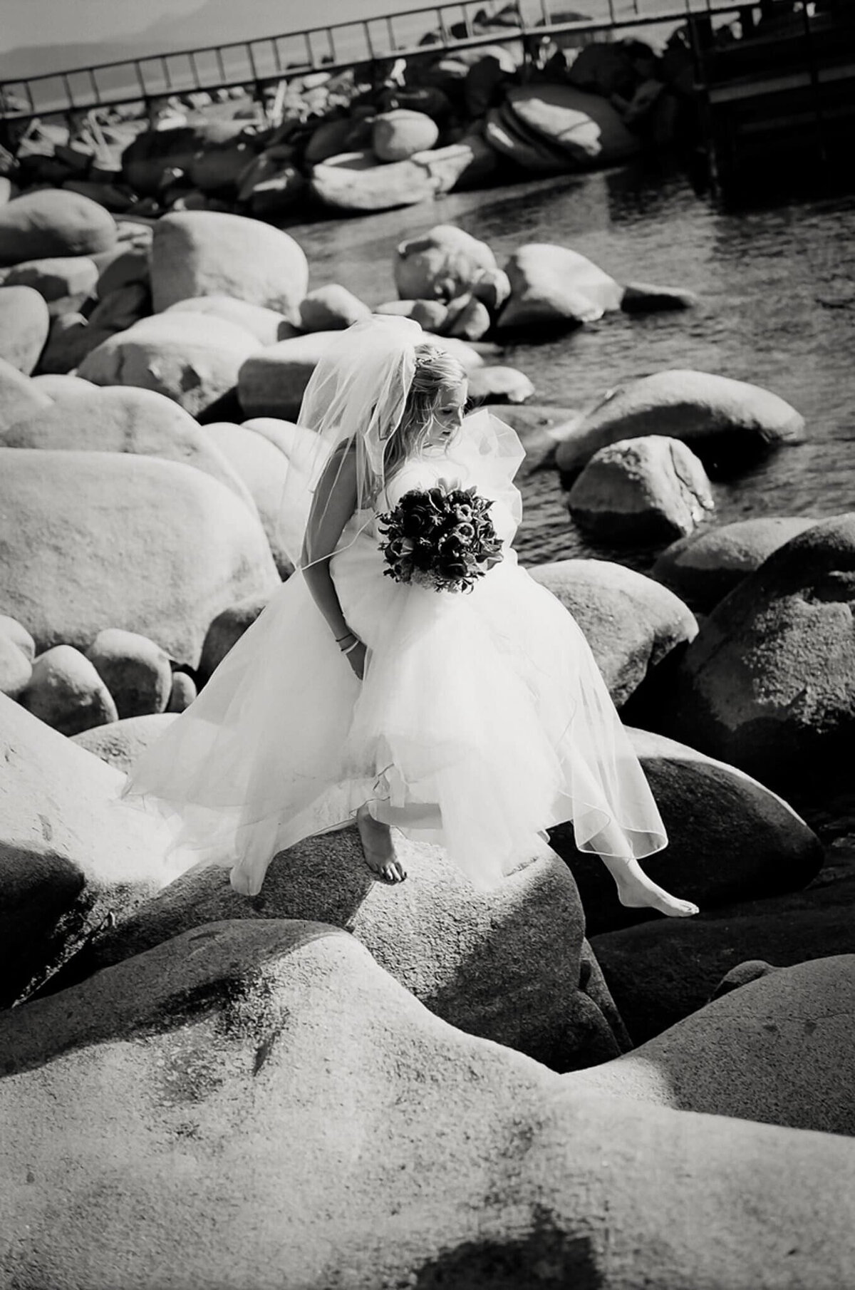 Bride jumping on boulders in her dress and bouquet. Black and white film image