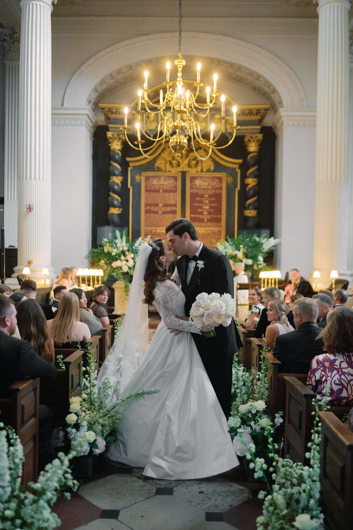 bride and groom kiss on their wedding aisle which is decorated with meadows of green and white flowers at their church wedding ceremony in london