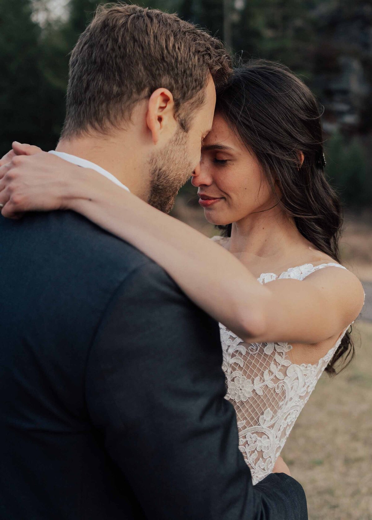 Maddie Rae Photography bride and groom standing face to face touching foreheads. she has her arms around his neck and his arms are around her waist. taken from behind the groom