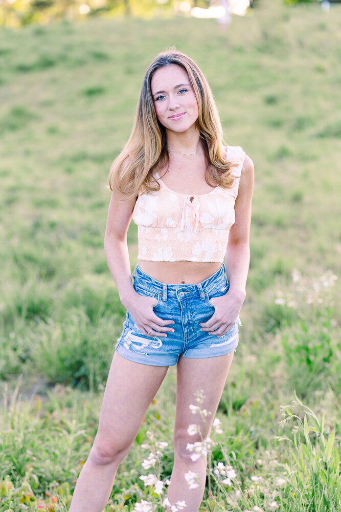 HIgh school senior girl in a field wearing jean shorts and cute top.