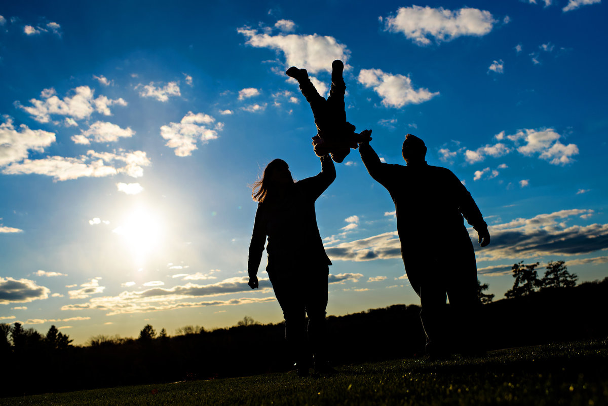 A silhouette of a family swinging their baby up in the air.