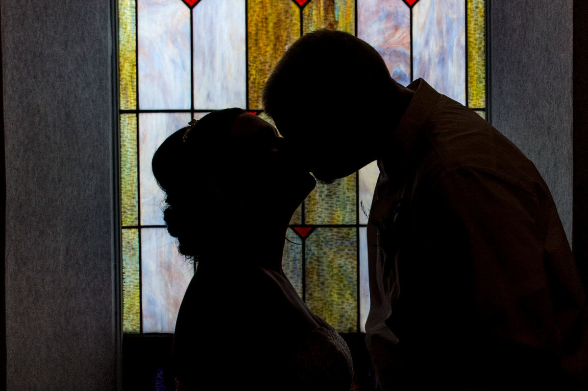 backlit bride and groom share kiss