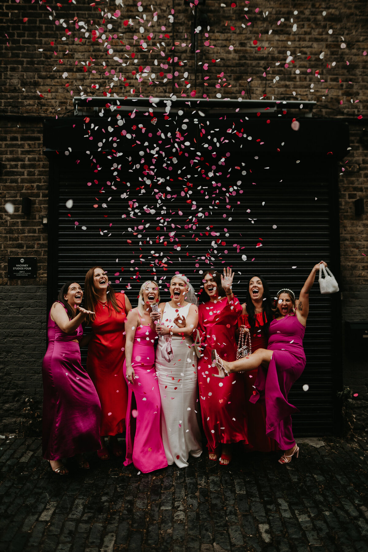 A bride and her bridesmaids wearing pink bridesmaid dresses let off a confetti canon at Clapton Country Club in London.