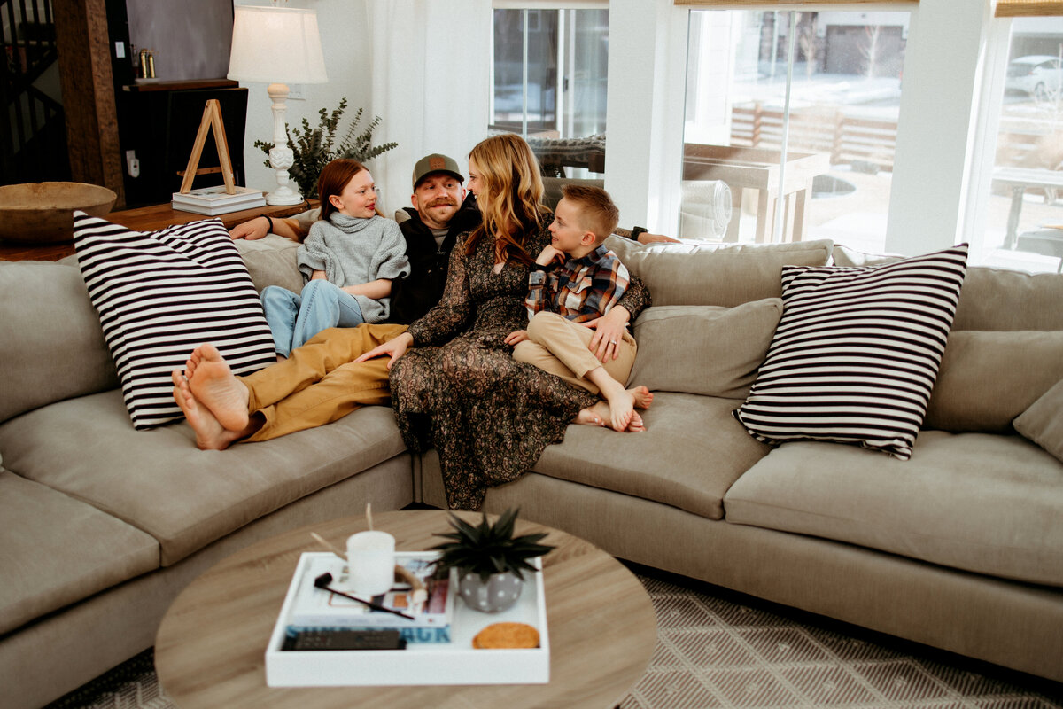 family of four cuddles on couch for at home family photos