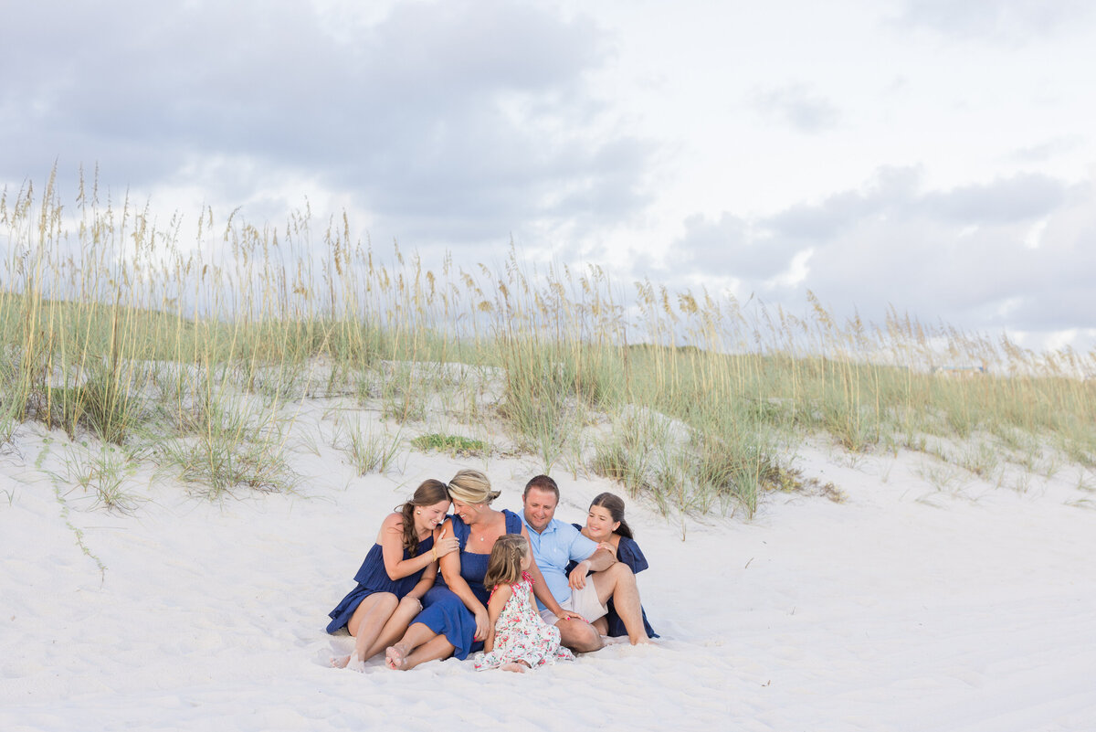 A family sitting close together in Inlet Beach, with a sand dune behind them.