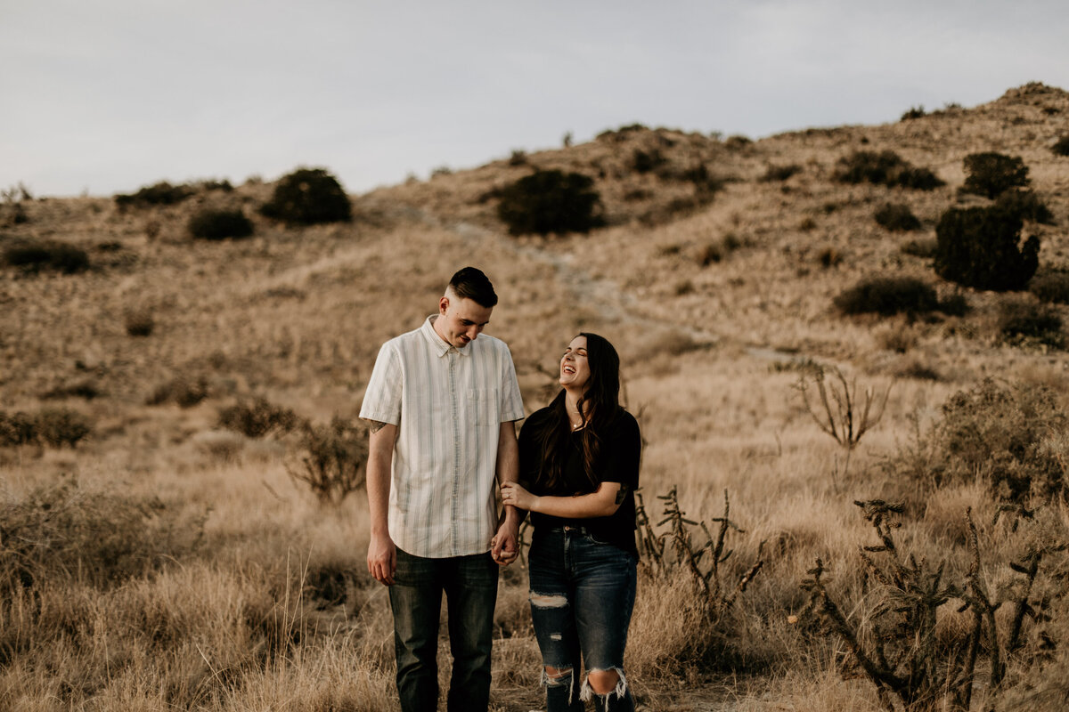engaged couple walking and holding hands laughing in the desert