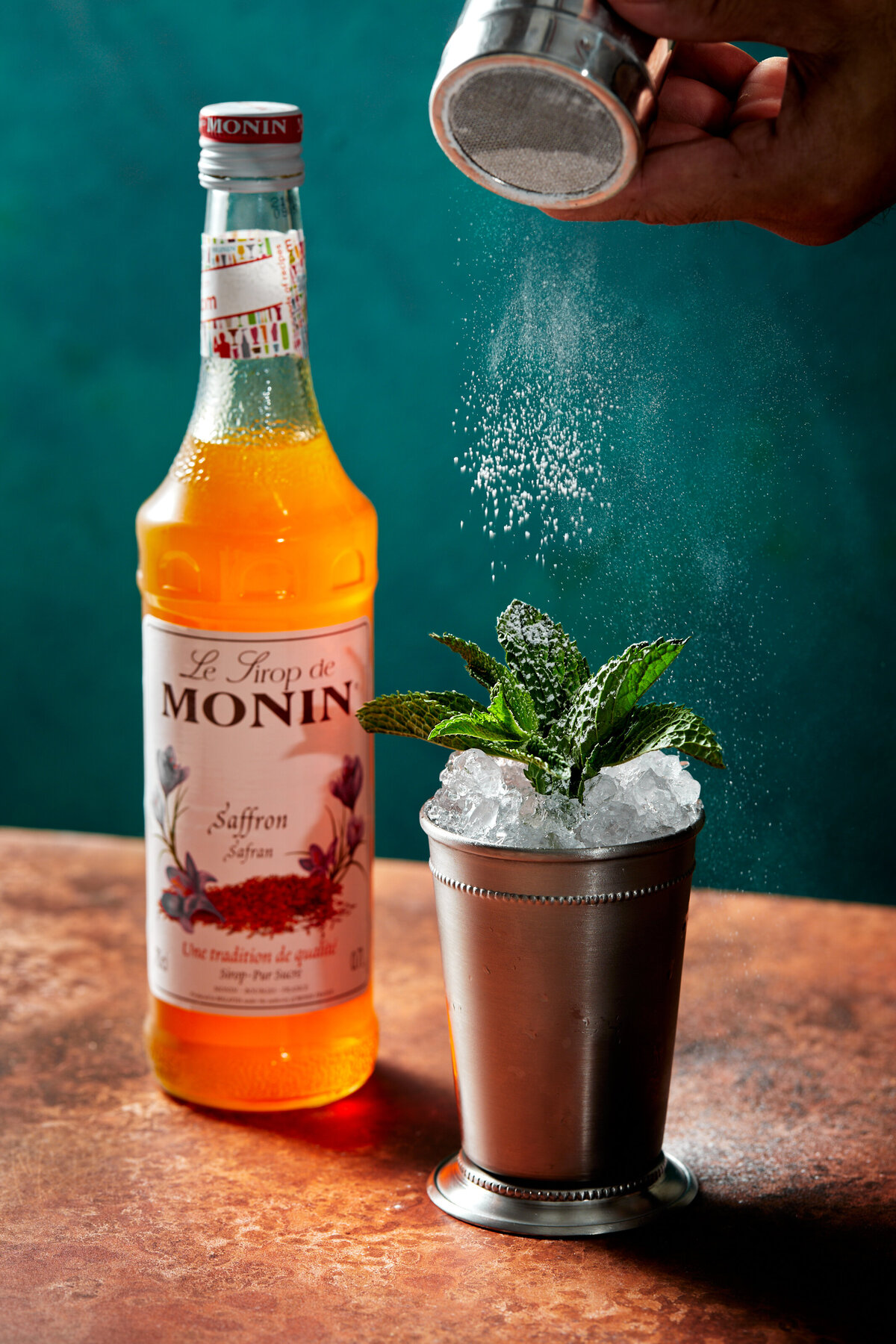 Sprinkling icing sugar on top of a saffron drink with a mint garnish.
