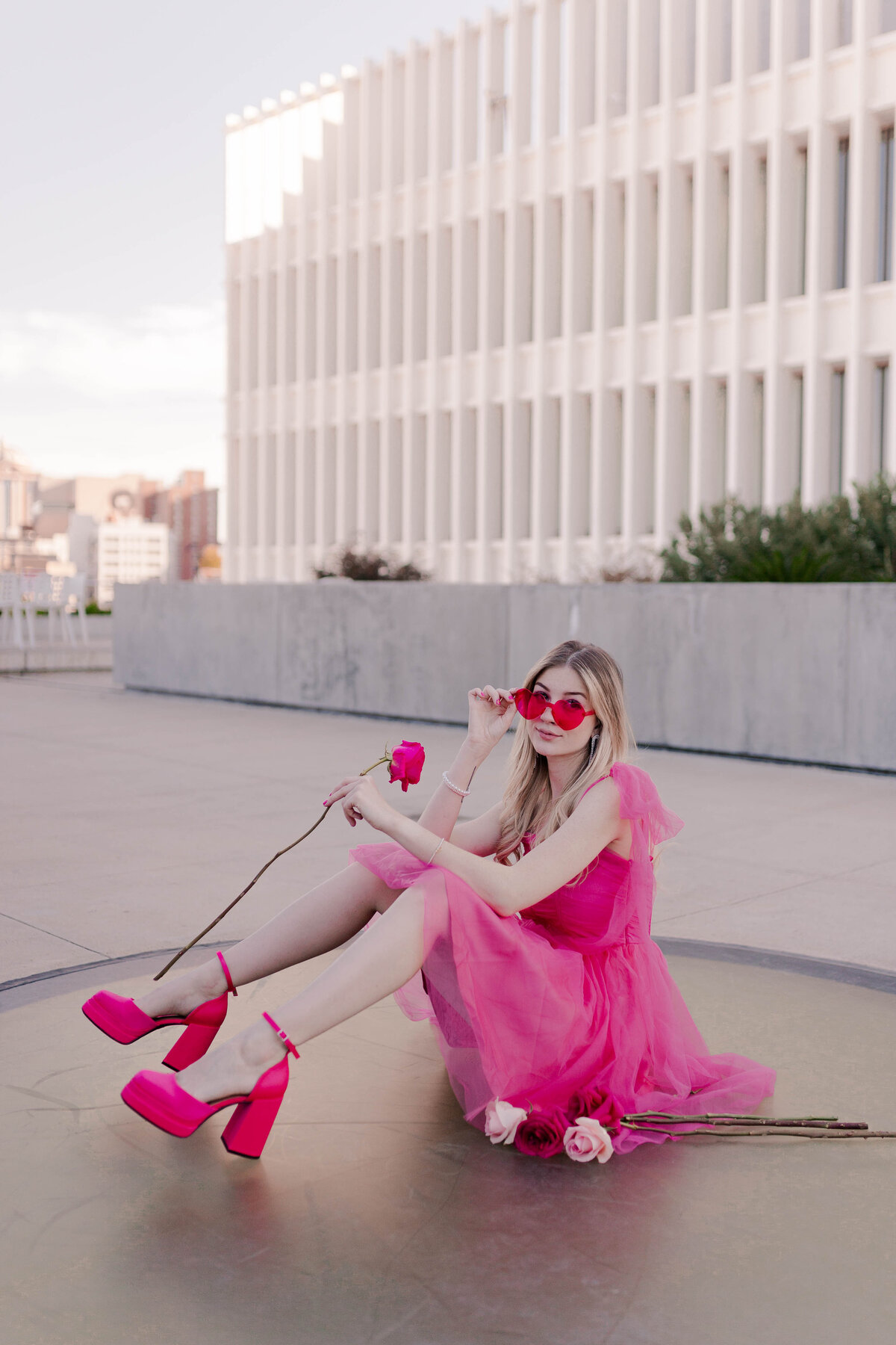 barbie model holds a pink rose while wearing hot pink heart-shaped sunglasses in rooftop in houston