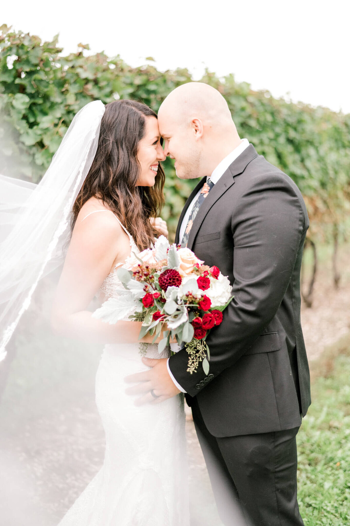 Bride and groom pose in vineyard with their foreheads touchings and looking into each others eyes