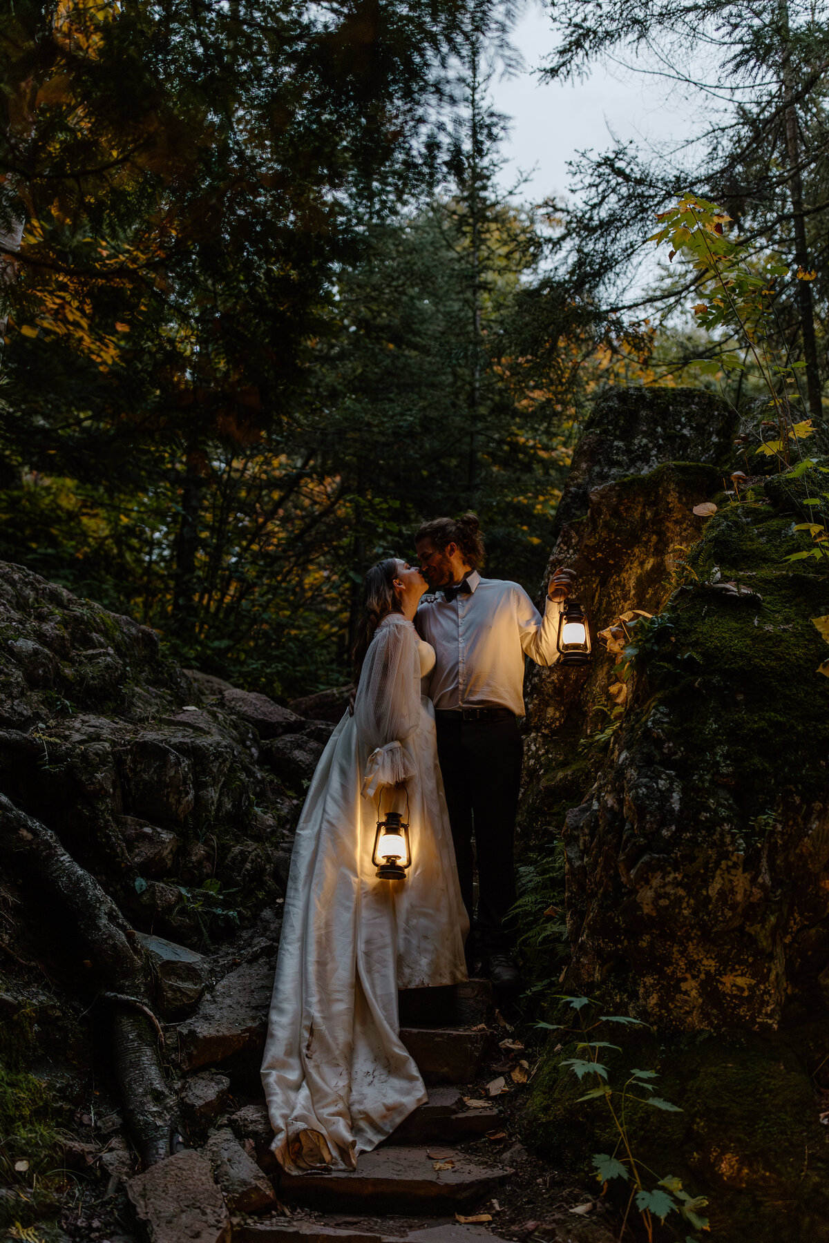 Bride and groom kissing while holding lanterns after dark during their temperance river state park mn elopement.