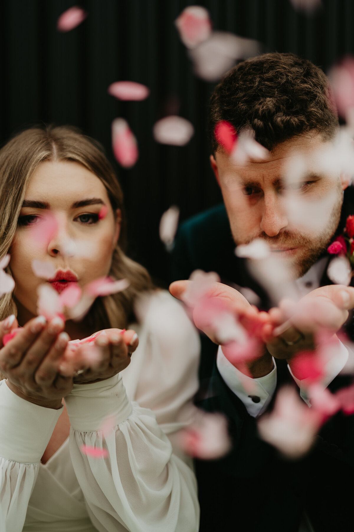 A Bride and Groom blow confetti at the photographer.