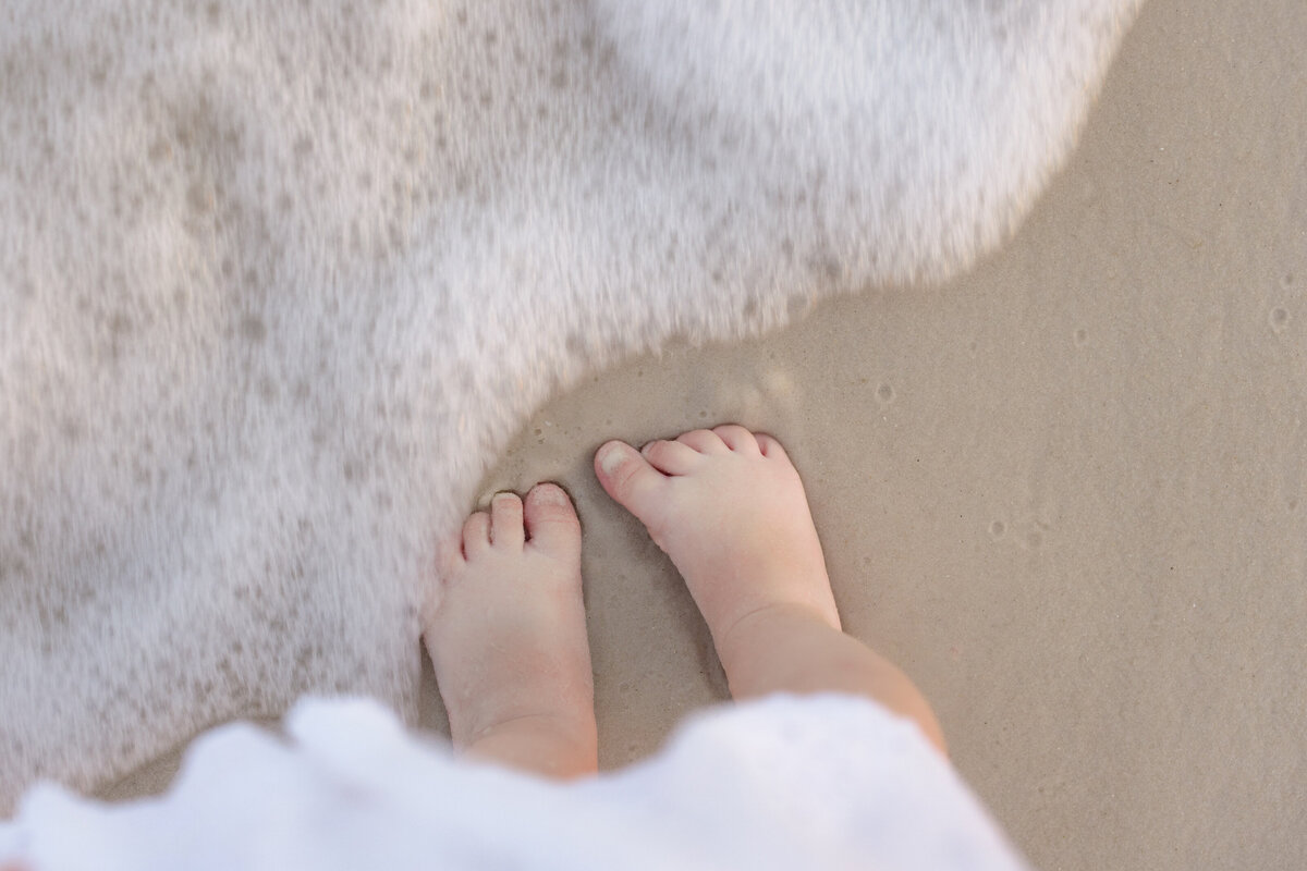 Close up of a small child's feet as a wave flows into it