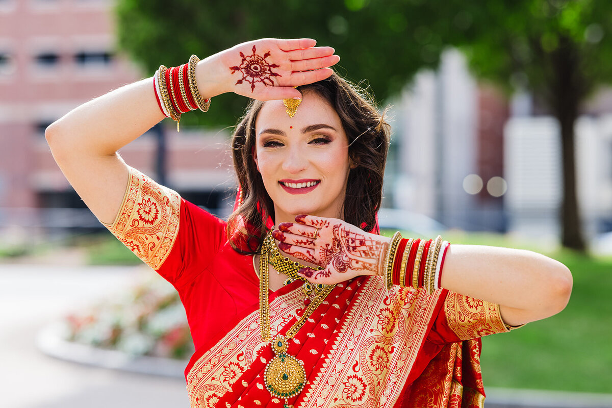 A joyous bride in a red saree with intricate henna designs on her hands and arms, showcasing her bridal jewelry.