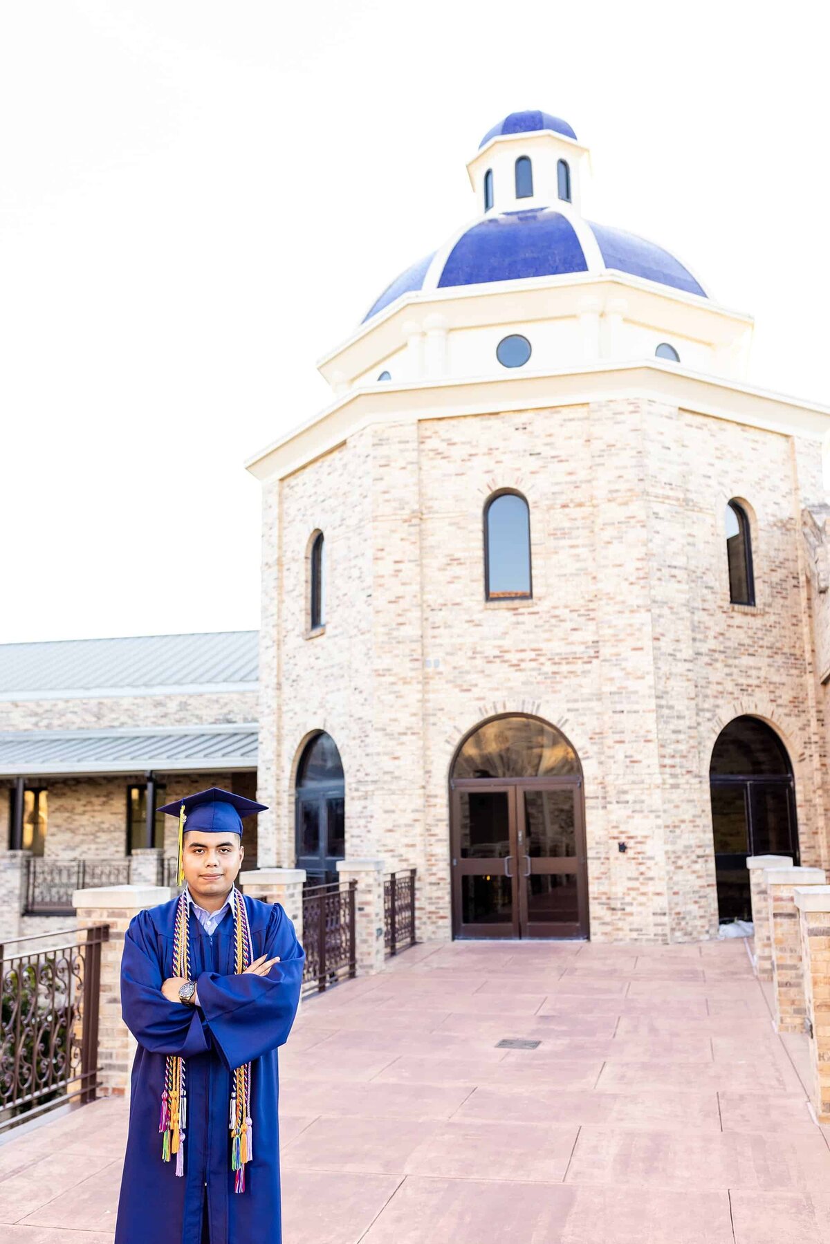 Senior posing in front of school in cap and gown