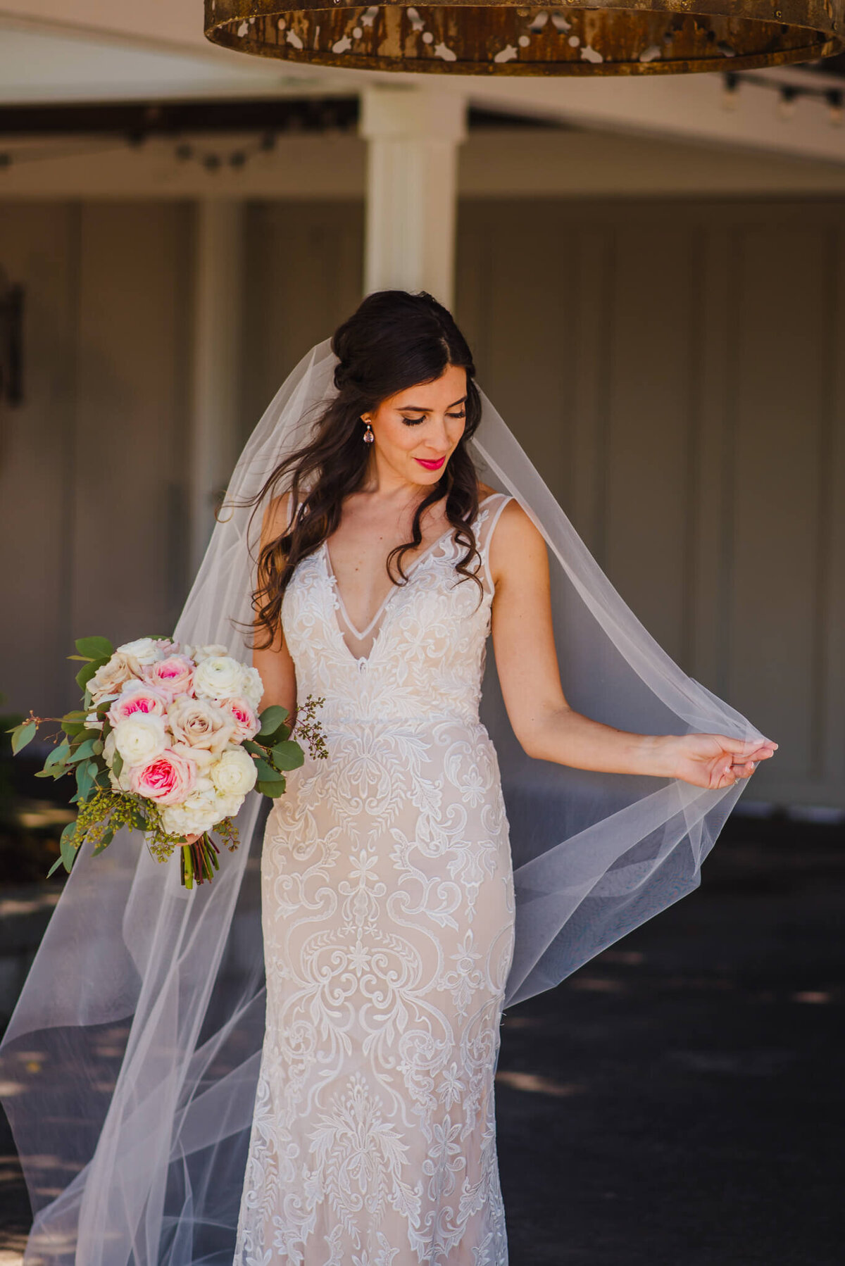 Photo of a bride holding a bouquet and playing with her wedding veil