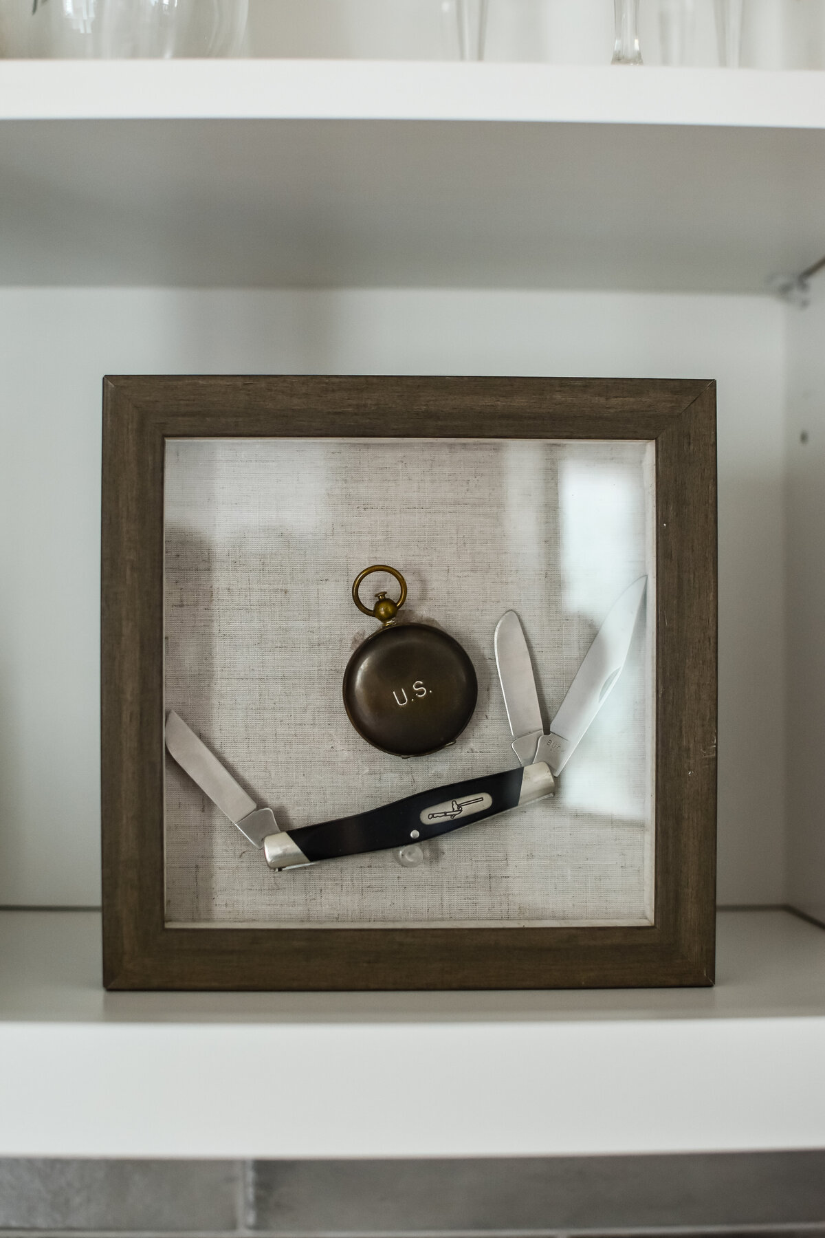 A pocket knife in a glass display case sits on a white shelf