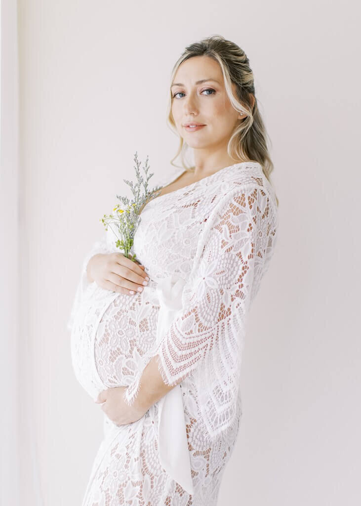 Mother holding flowers in a lacey white maternity dress.