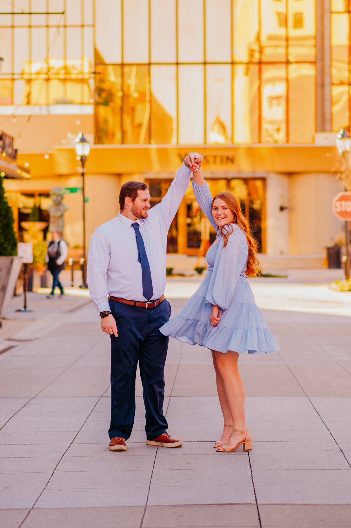 photo of a woman spinning with her fiance in front of a fancy hotel