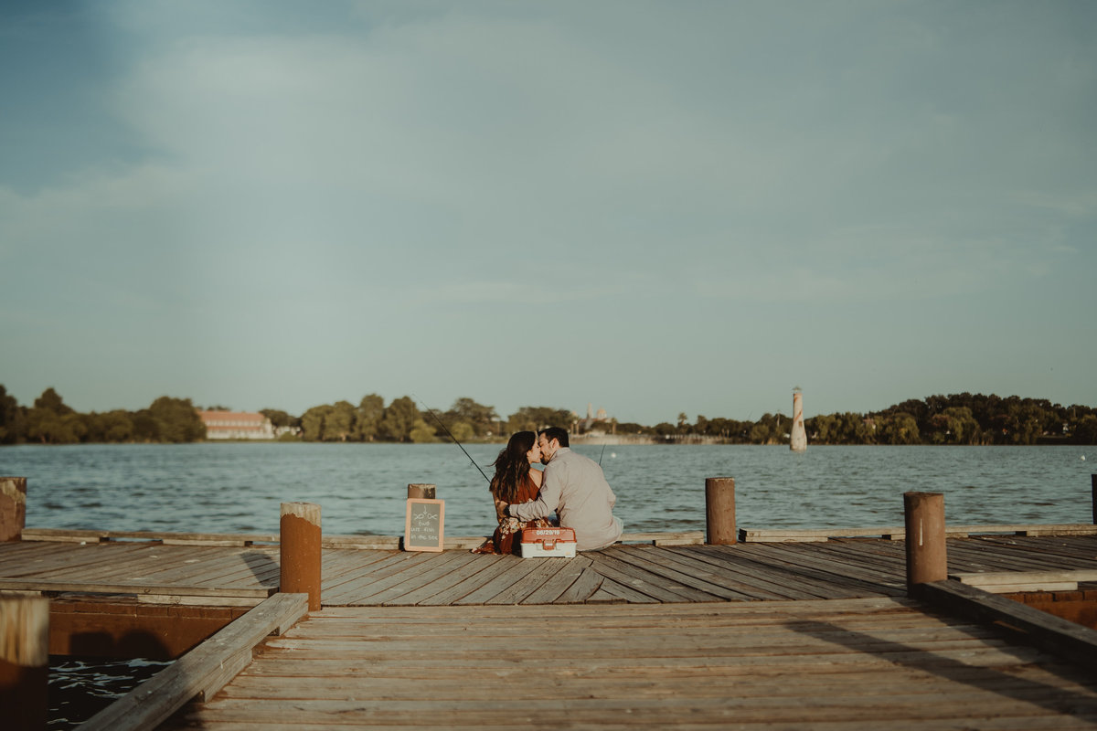 Couple kissing on the edge of a fishing pier on their engagement session by Expose The Heart Photography.