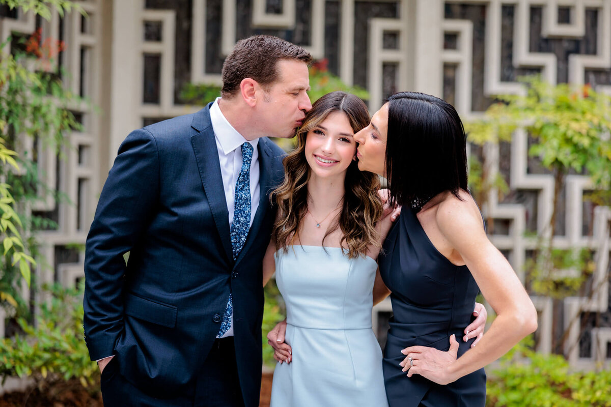A mother and father kiss their daughter on either side while standing in a garden for some Bellevue Bar and Bat Mitzvah Photography