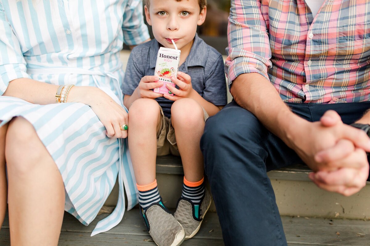 A little boy sipping his juice box while sitting between his Mom and Dad during a lifestyle photo session.