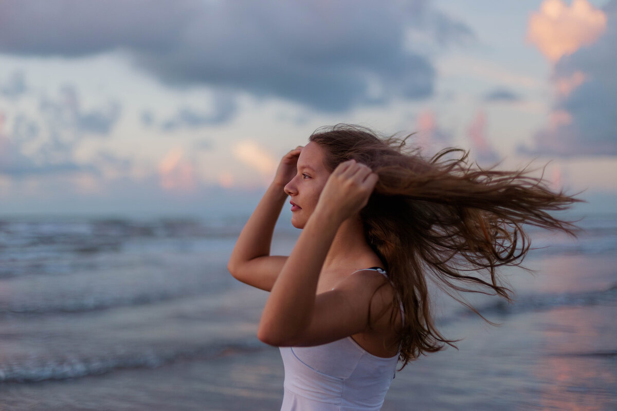 A young girl stands on the beach facing the sunrise while the wind blows through her hair in Galveston Texas