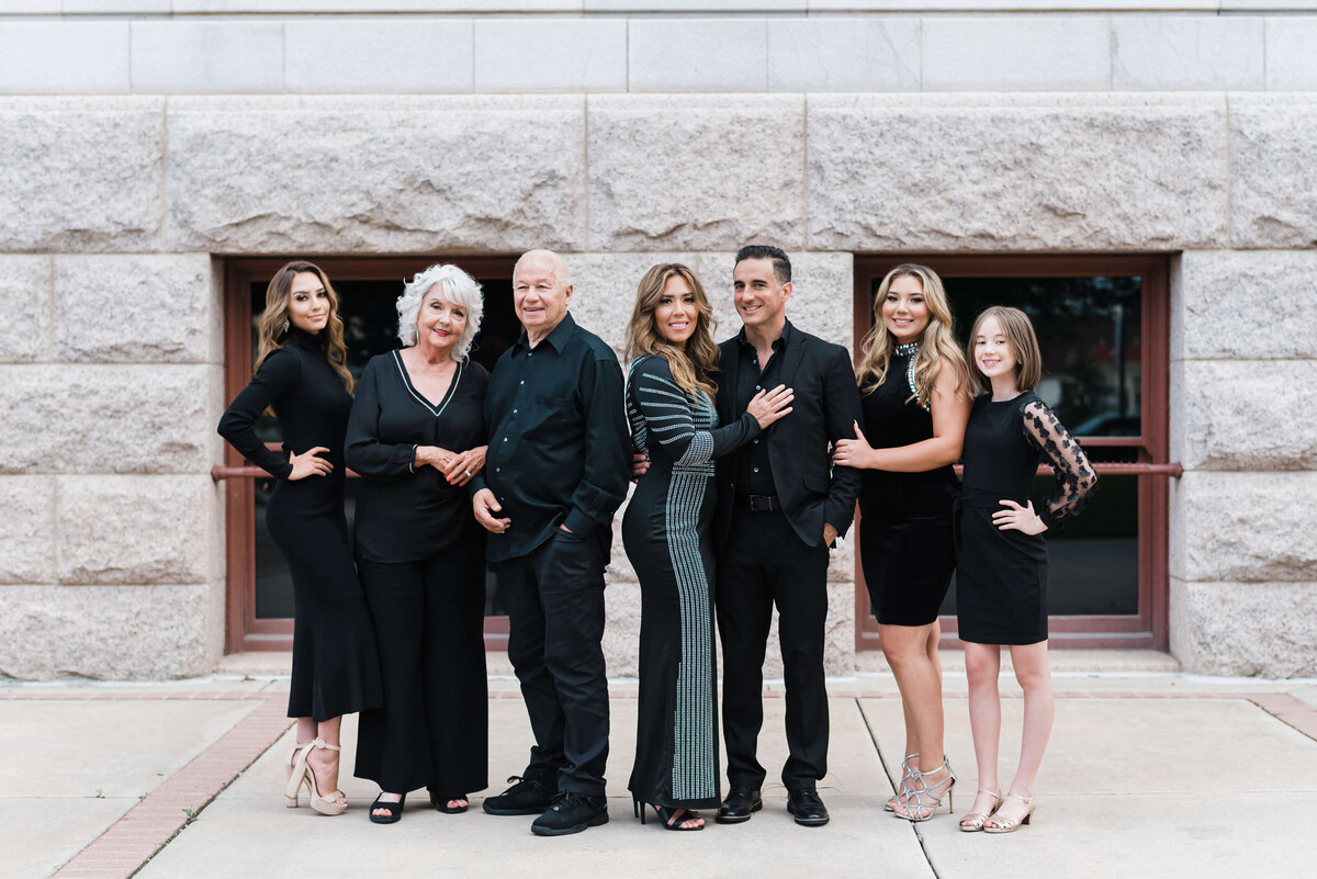 An attractive family stands in front of a white building downtown while dressed in all black