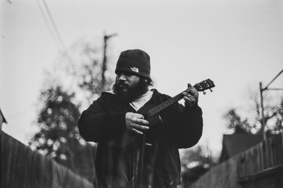 David Castillo wearing a North Face beanie and playing a ukulele in an alley