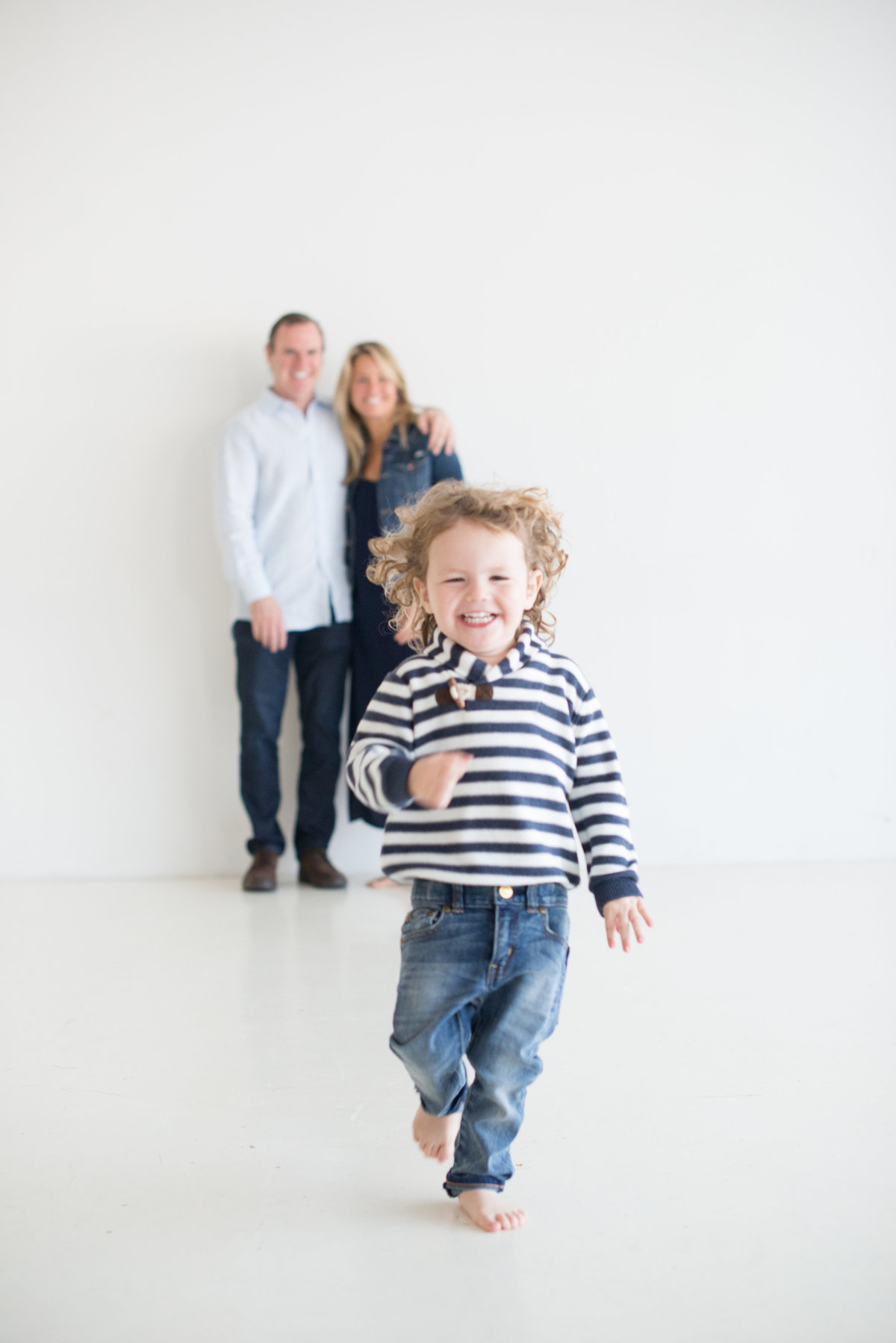 little boy running in front of parents at white photography studio