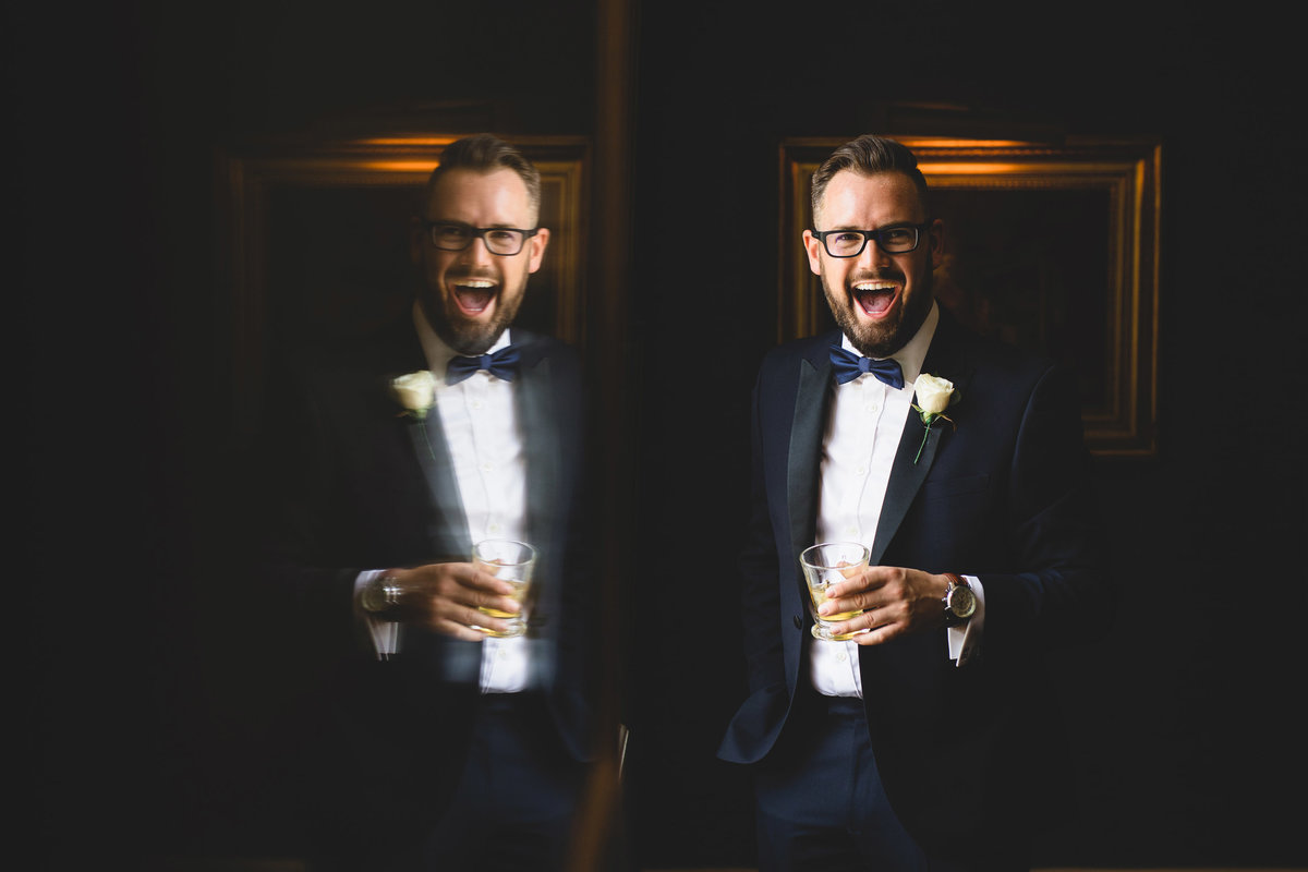 The groom and the Tuxedo is holding a glass of whiskey on his wedding day