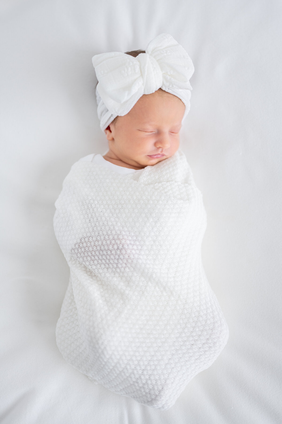 Newborn baby wrapped in a blanket and wearing a large bow on her head