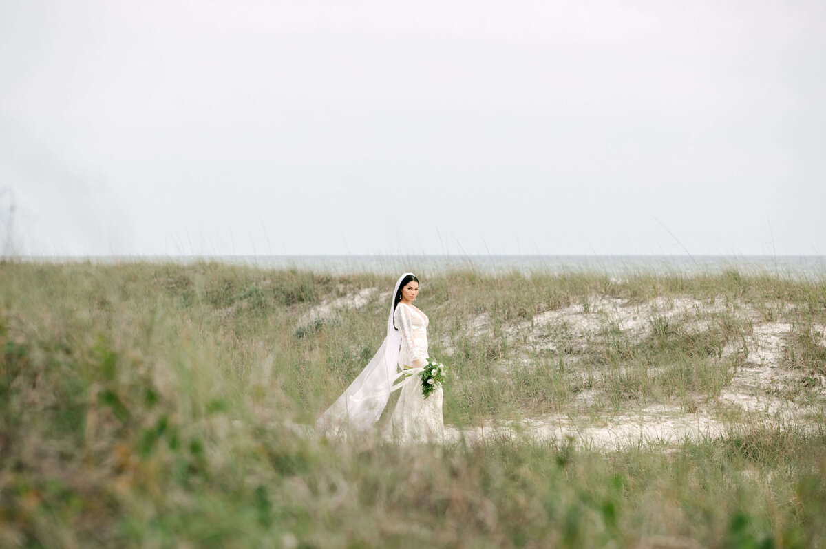 bride on beach path in wedding dress - surrounded by coastal grass with the gulf of mexico in the background.  Photographed by Panama City Beach photographer Brittney Stanley of Be Seen Photos